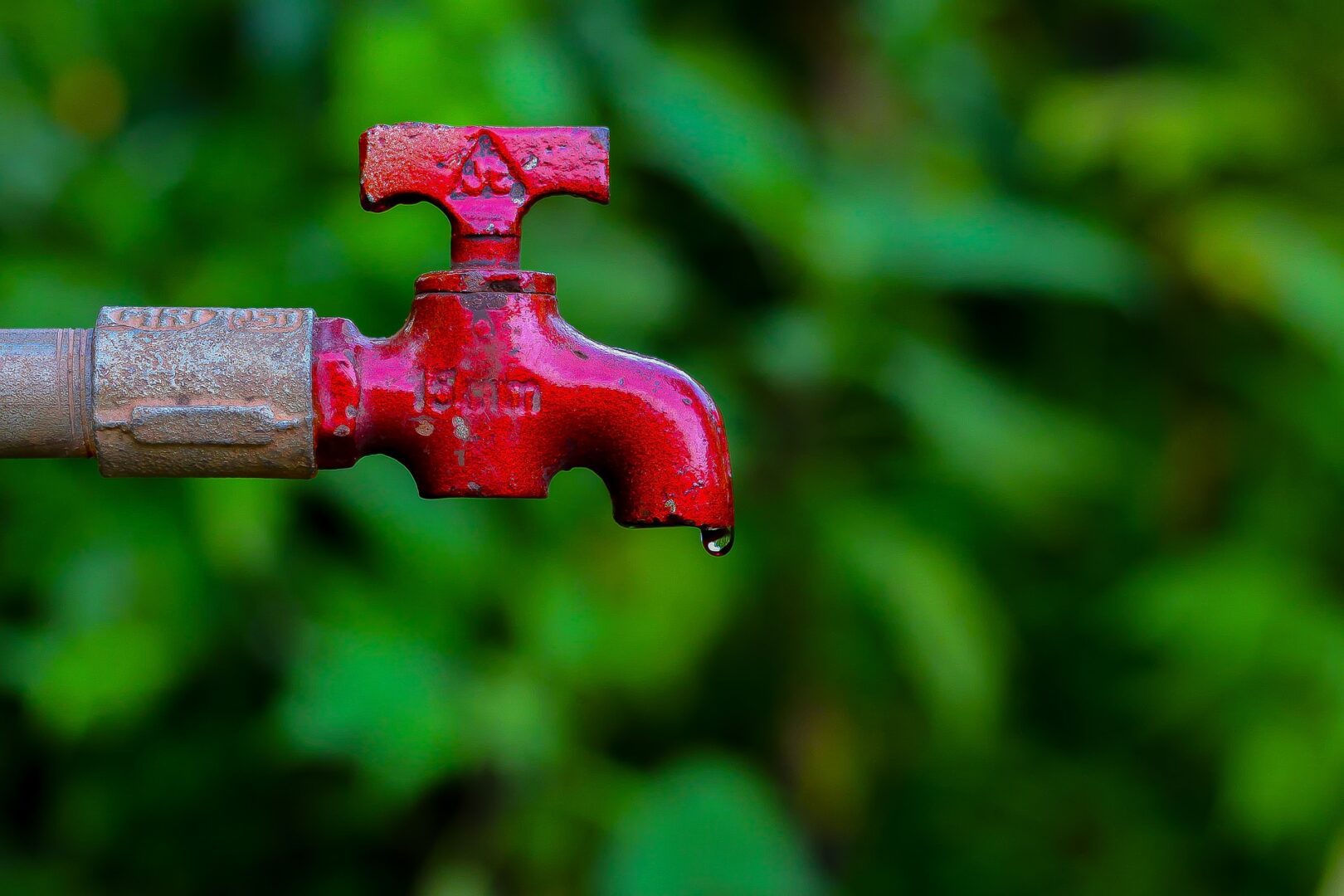 A red faucet is leaking water from the side of it.